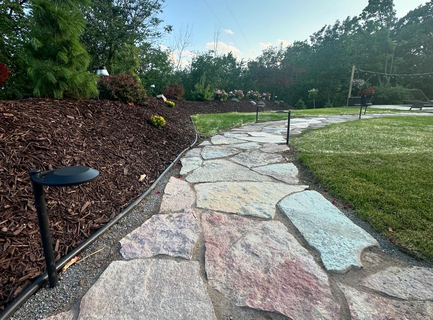 Paver patio and walkway installed beside a landscaped yard